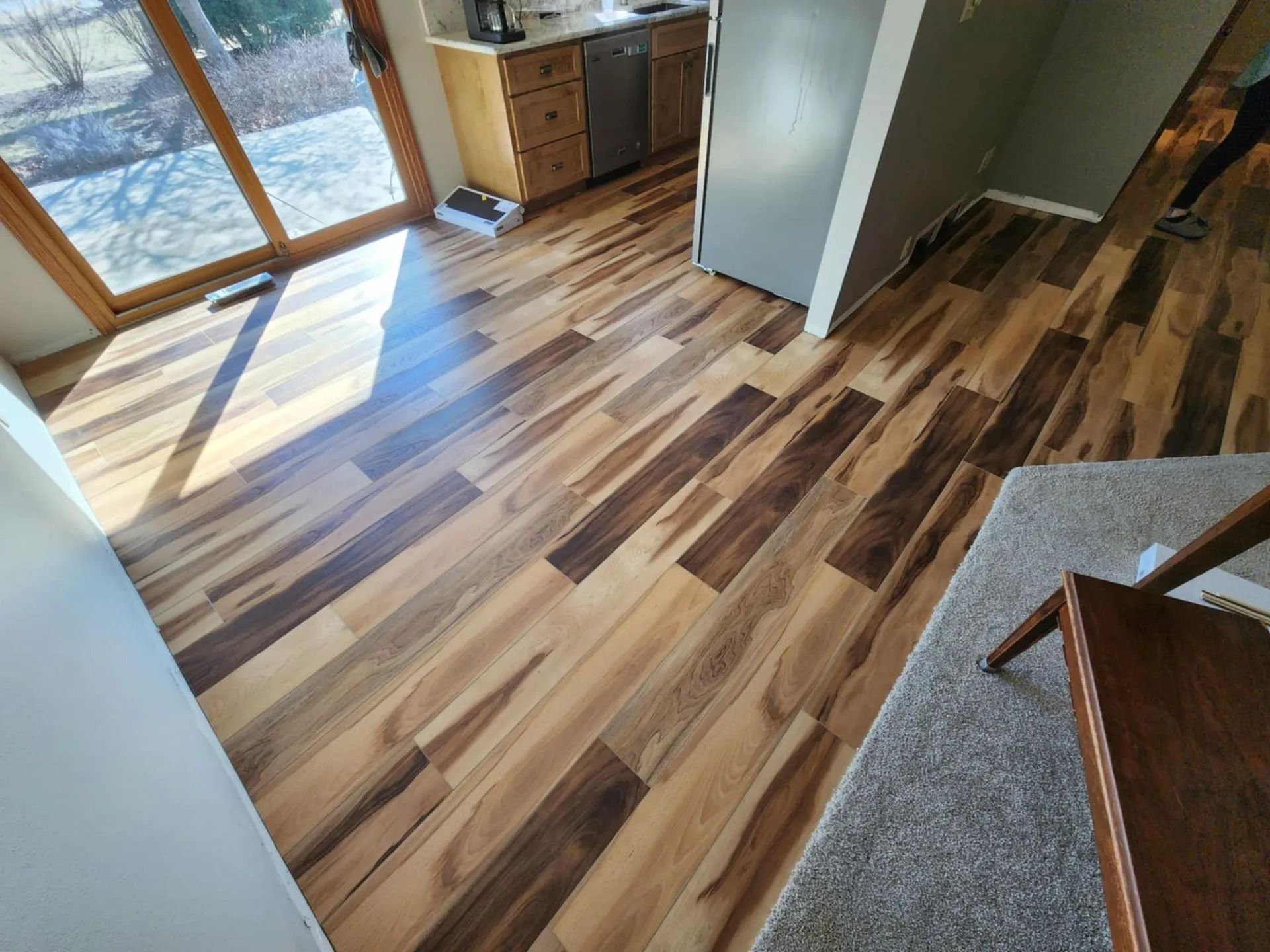 Sunlit room with striped hardwood floor, large windows, a cabinet, and carpeted stairs.