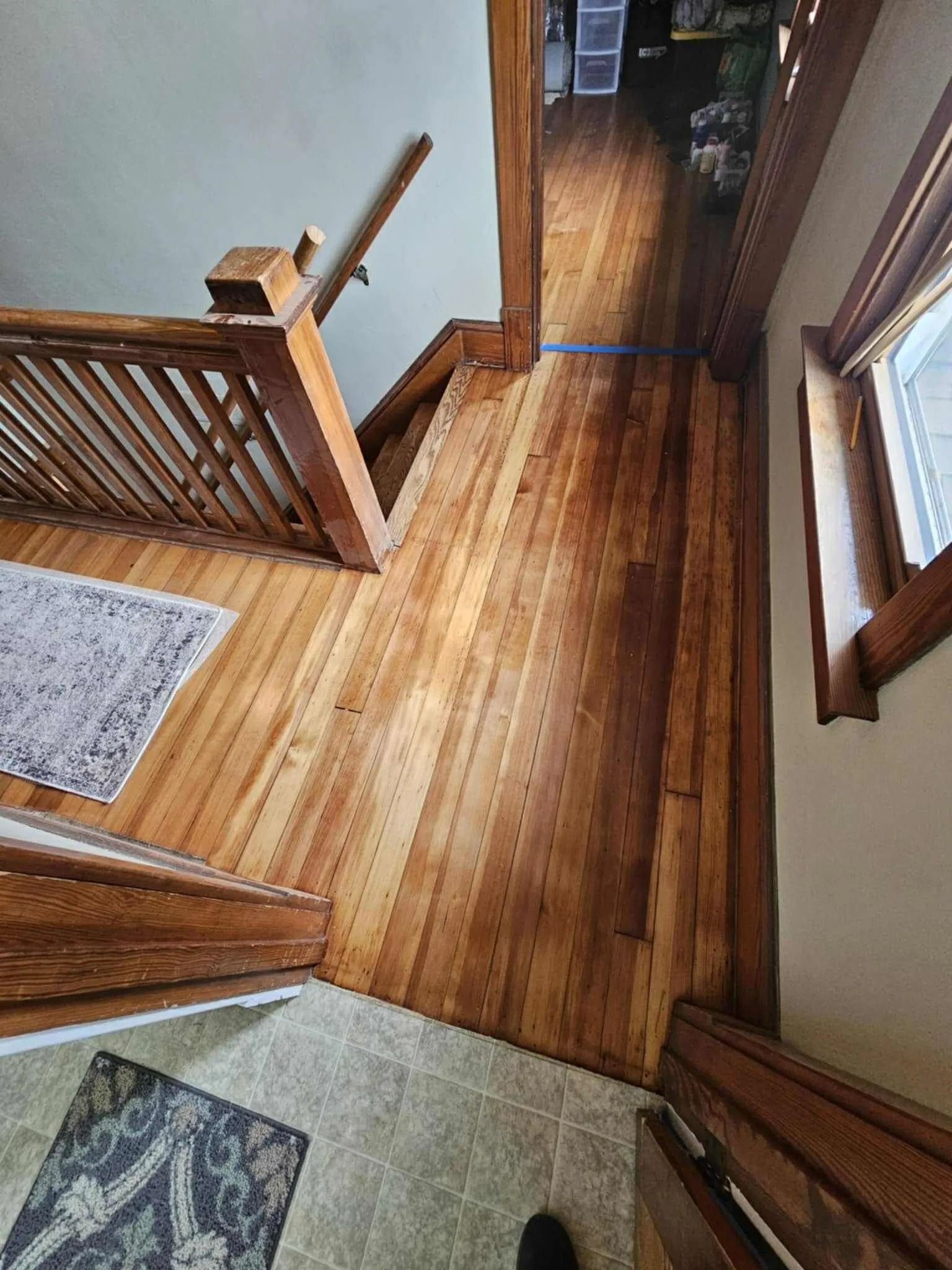 Wooden hallway with staircase railing, polished floor, and sunlight from a window