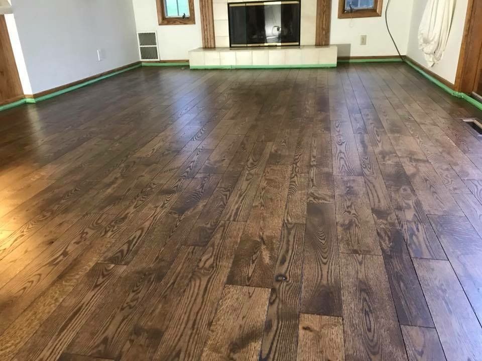 Empty room with dark hardwood floors, a fireplace, and windows with curtains along the back wall