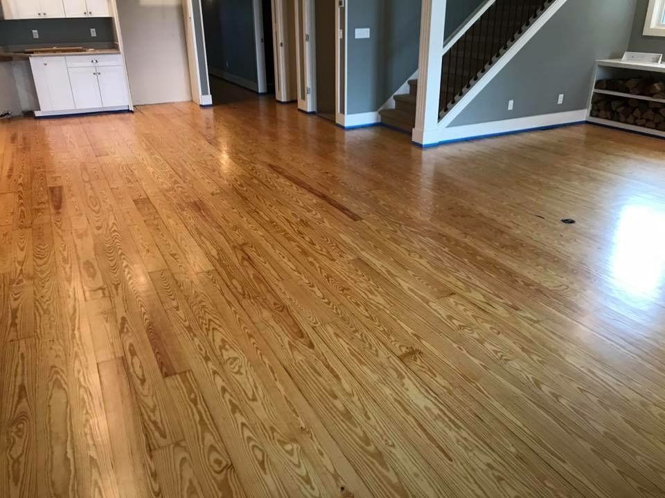 Empty living room with hardwood floors, gray walls, stairs, and a small kitchen area in the background