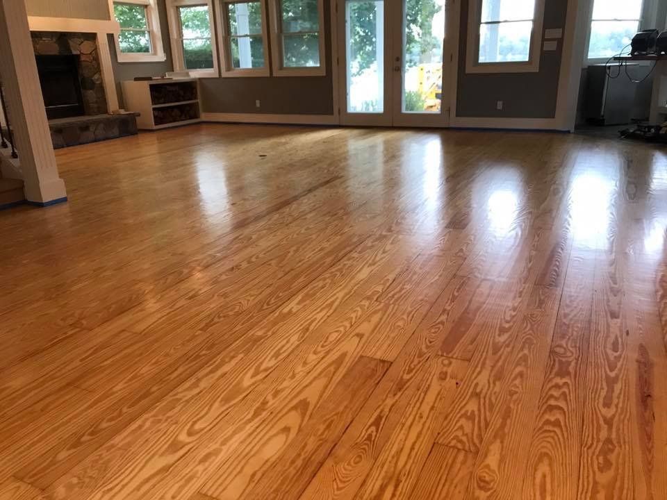 Empty hardwood living room with large windows and a fireplace