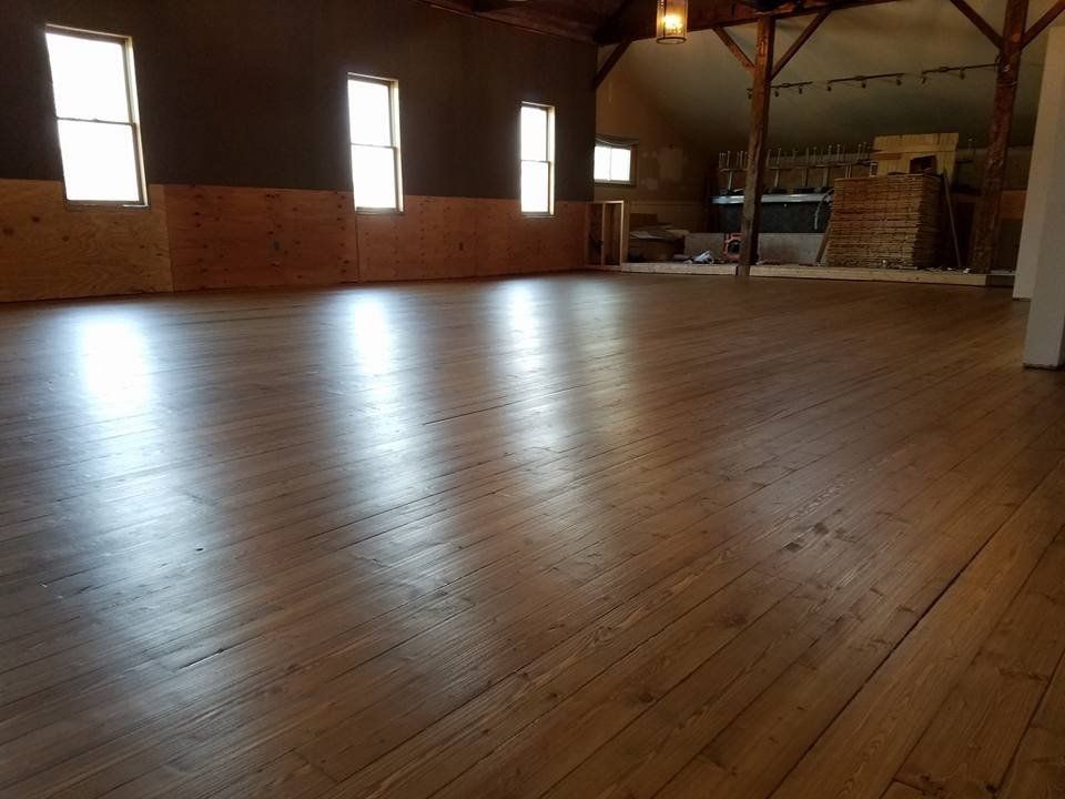 Empty wooden-floored room with brick walls and tall windows, lit by sunlight.