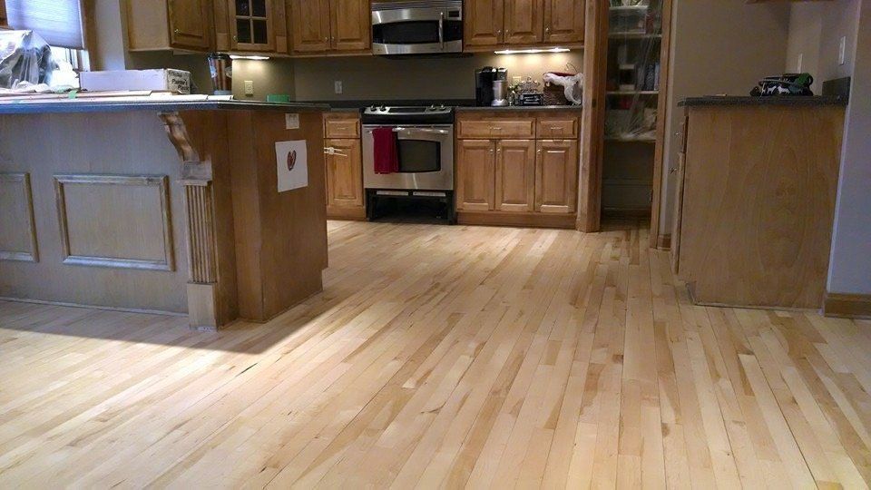 Empty kitchen with light wood floors, wooden cabinets, and a stainless-steel oven.