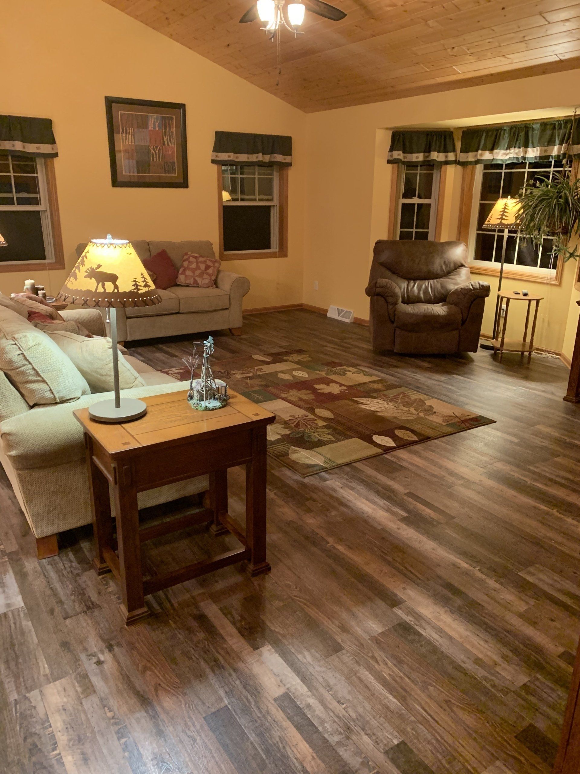Warm living room with sofa, armchair, lamp, coffee table, and patterned rug on wood floors.