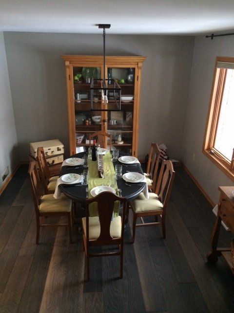 Dining room with set table, dark floors, wooden cabinet, and chairs by a window.
