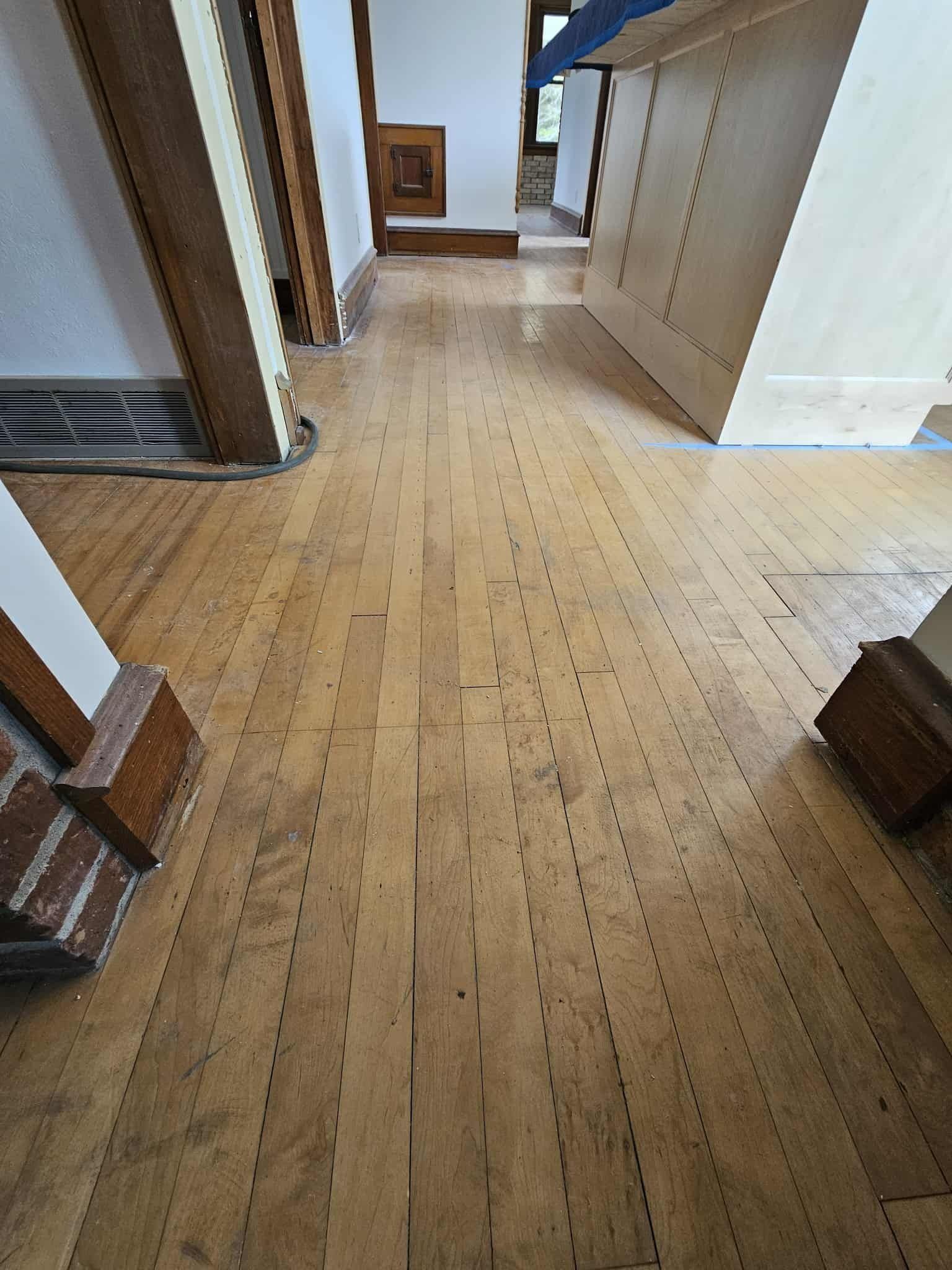 Wooden hallway floor with white walls, doorways, and built-in cabinets in a home interior.