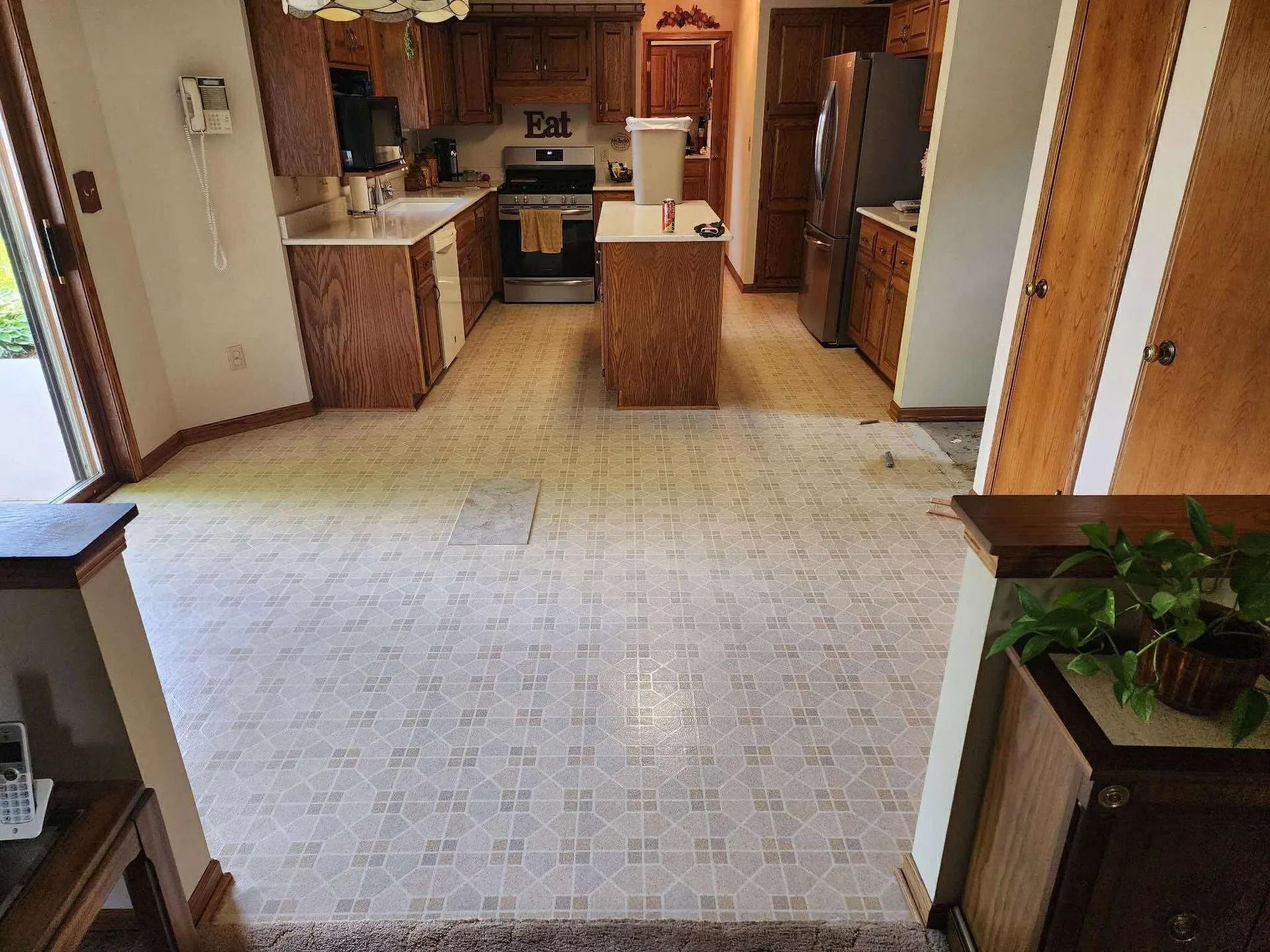 Empty kitchen with wood cabinets, white appliances, and beige carpeted floor.
