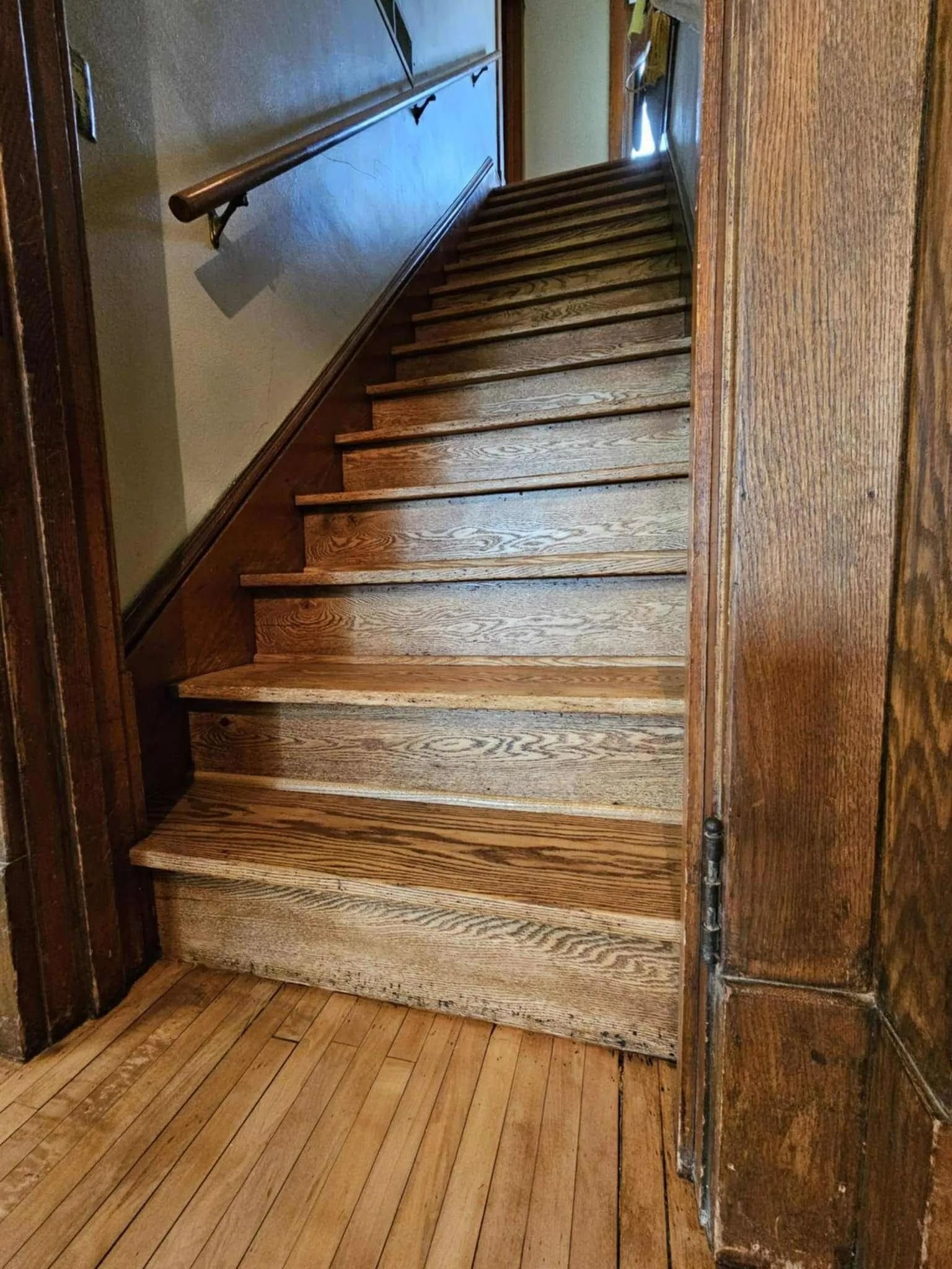 Wooden indoor staircase with worn steps and handrails in a narrow hallway