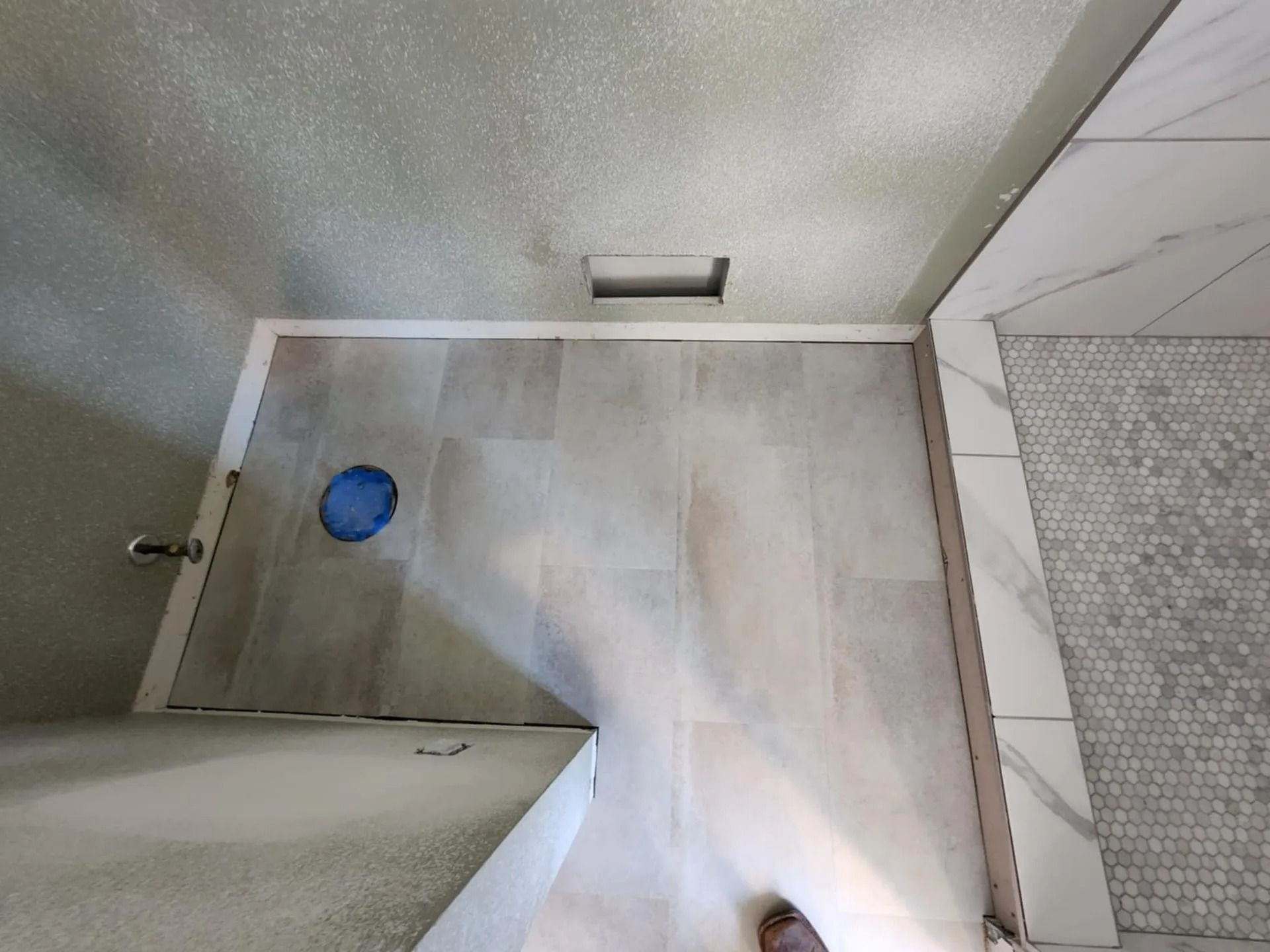 Small tiled bathroom with a shower drain and blue drain cover, viewed from above.