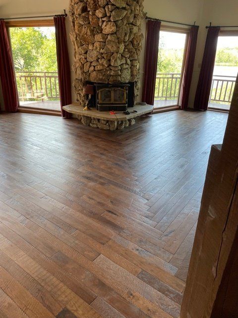 Empty living room with hardwood floors, stone fireplace, and large windows overlooking a balcony