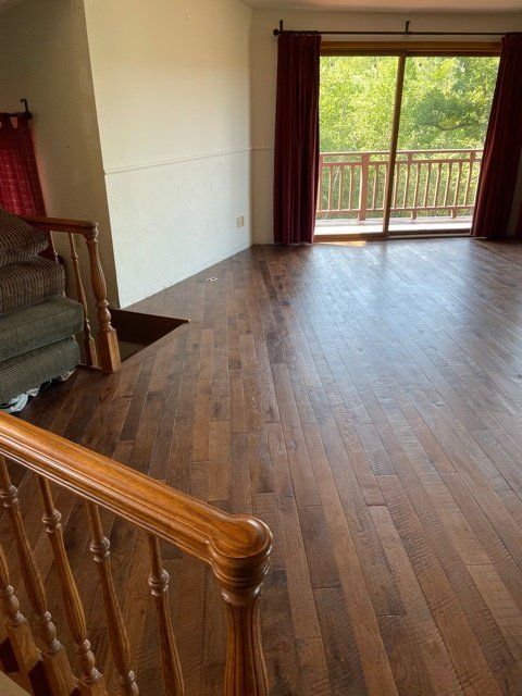 Empty room with dark wood floors, red curtains, and a balcony doorway overlooking greenery
