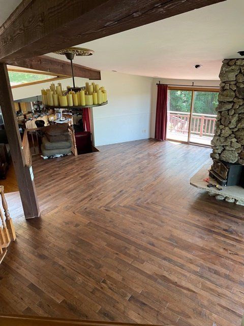 Spacious living room with wood floors, exposed beam, stone fireplace, and sliding doors to a balcony.