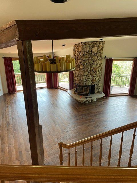 Open living room with wood floors, stone fireplace, and large windows overlooking a balcony.