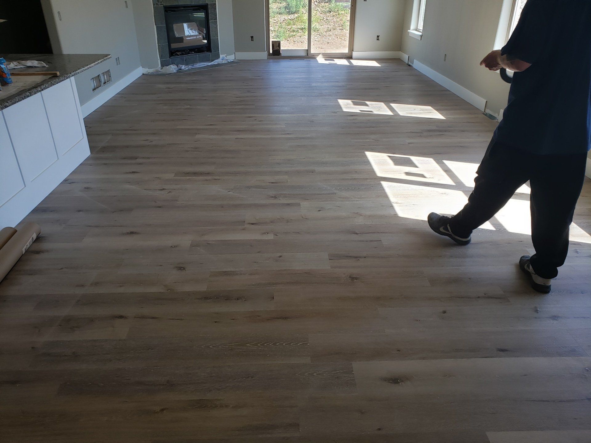 Empty living room with light wood floors, a fireplace, and a person standing near the right wall