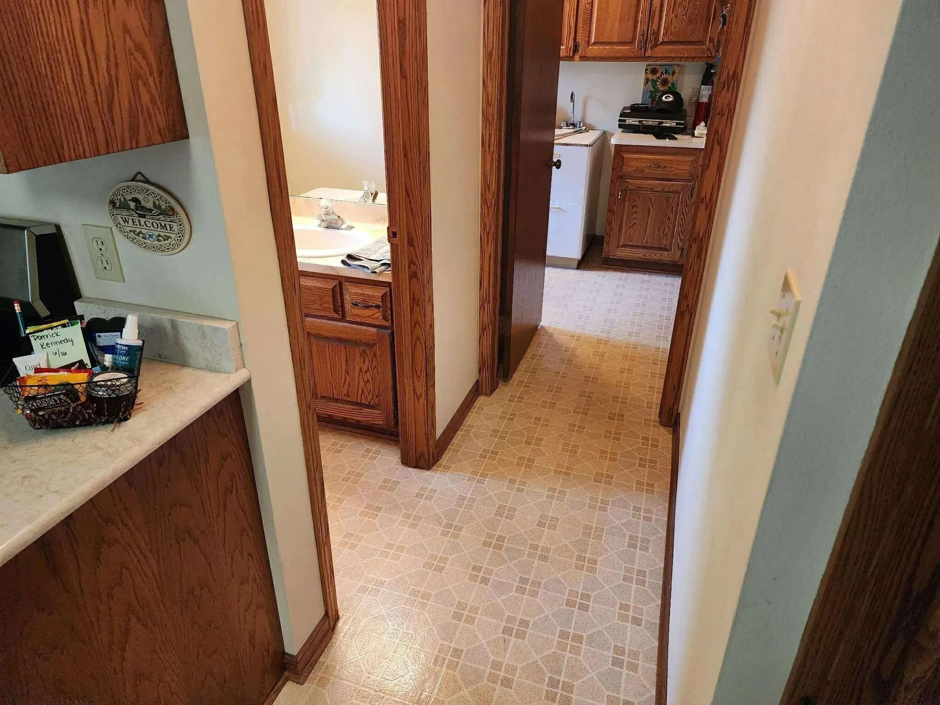 Narrow hallway with wood cabinets, beige tile floor, and a kitchen visible at the end