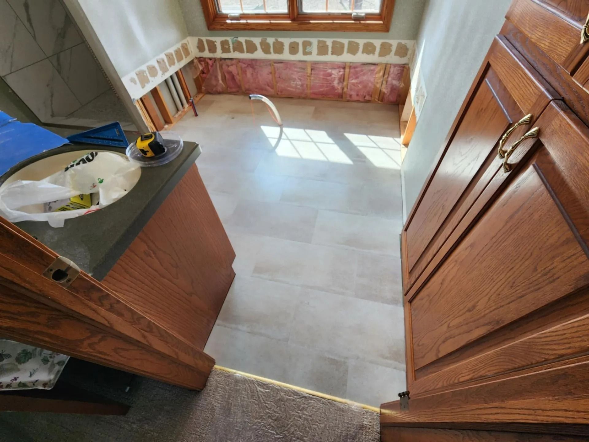 Wooden cabinets framing a tiled kitchen floor with sunlight streaming in from a window