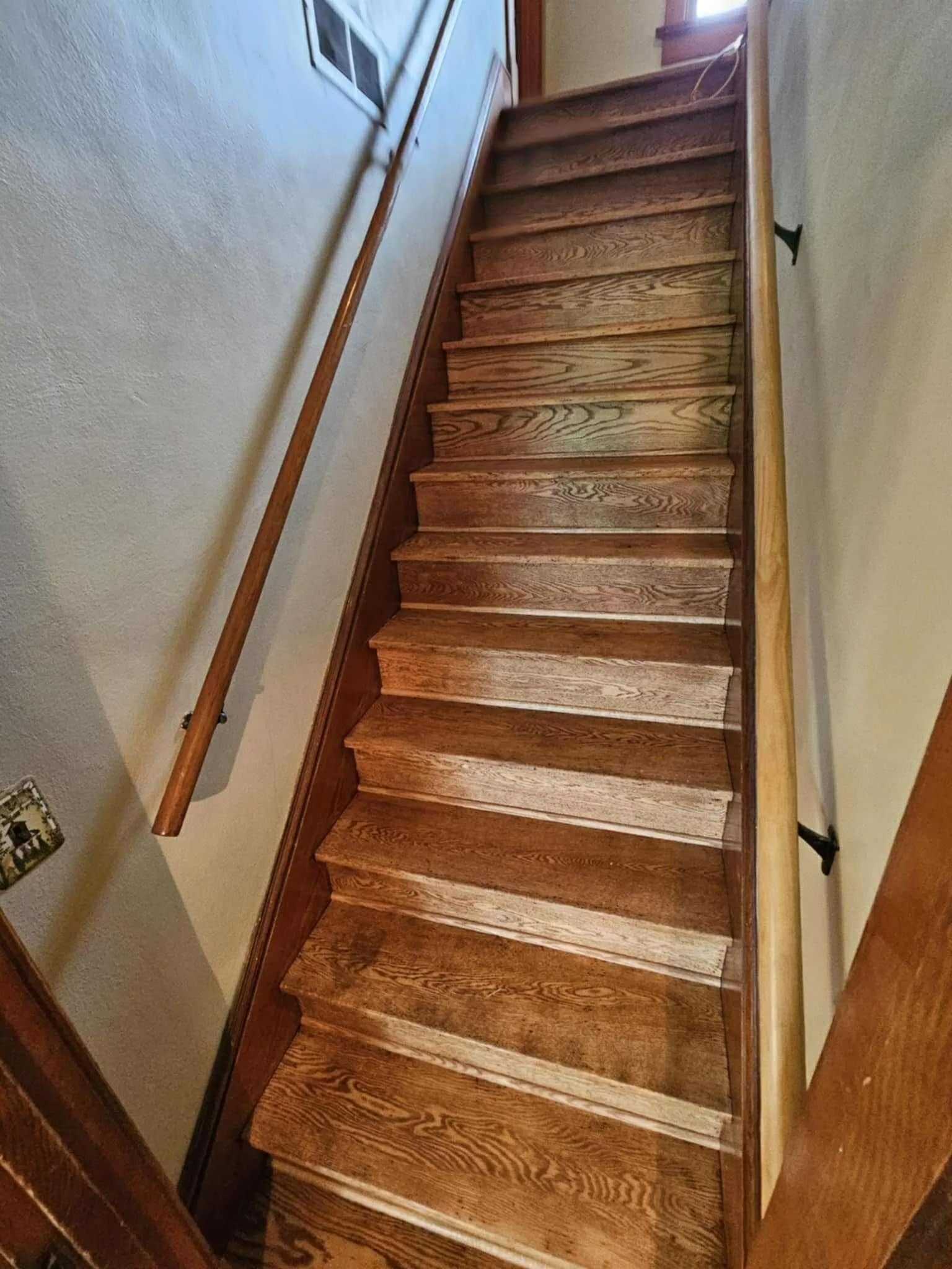 Narrow indoor staircase with brown carpeted steps and wooden handrails between light-colored walls