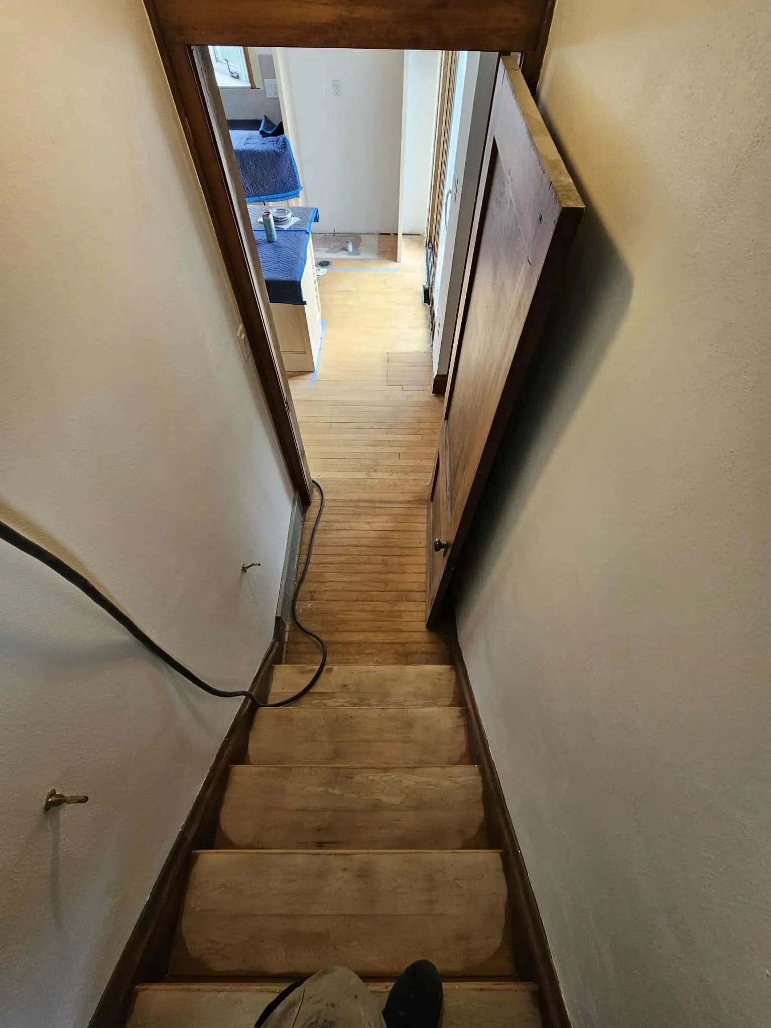 Narrow indoor staircase with beige carpet, wooden railings, and a hallway at the bottom.