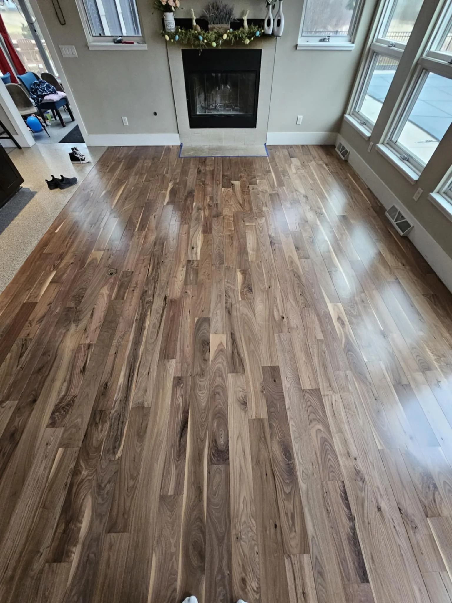 Bright wood-floored living room with a fireplace and large windows on the right.