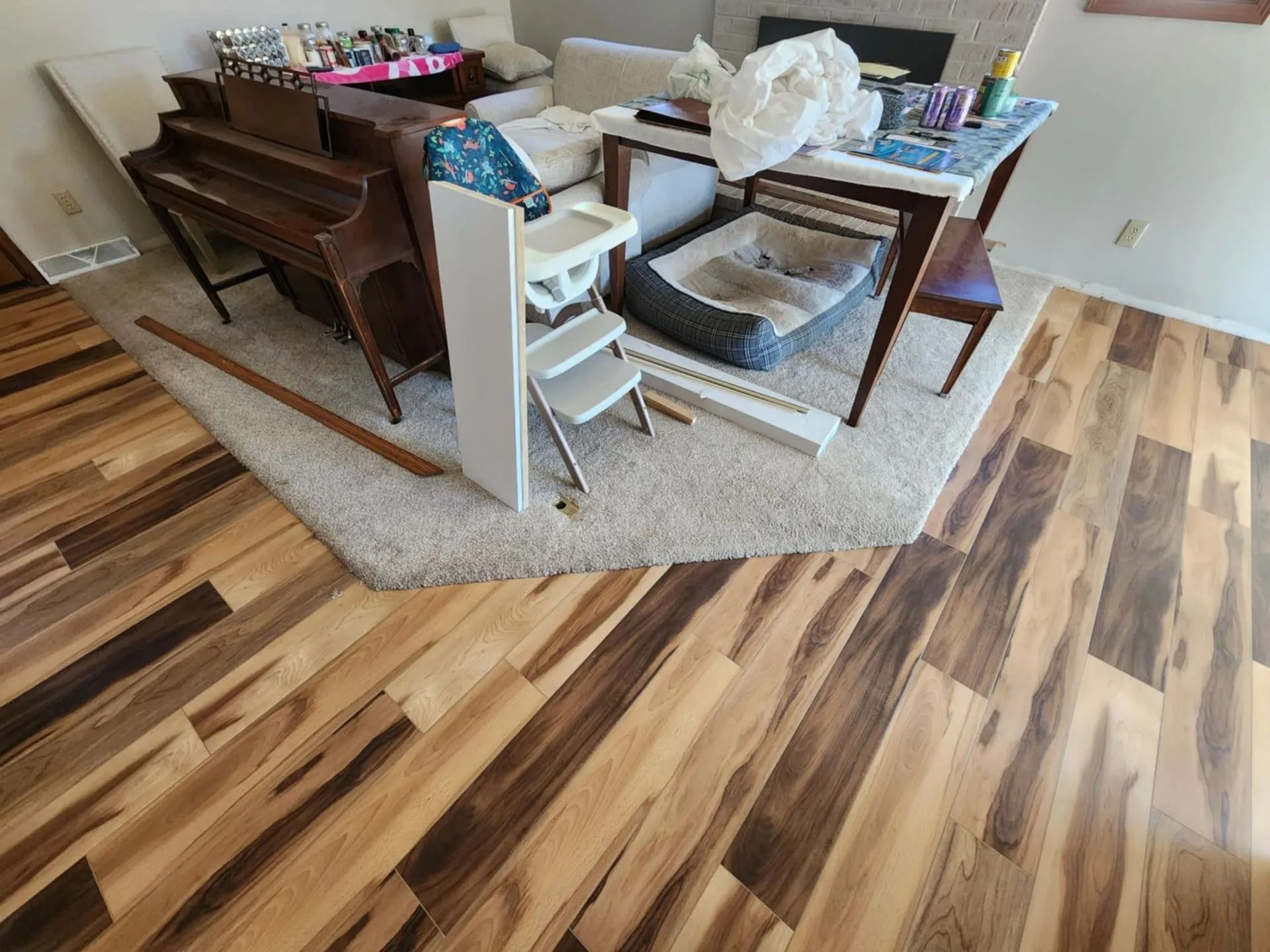 Living room with hardwood floor, area rug, piano, and cluttered table and chairs