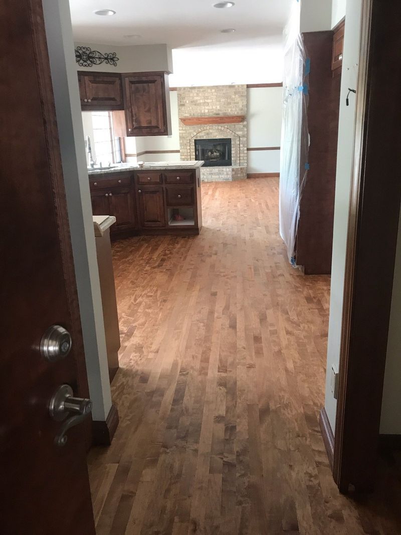 Kitchen and living area with wood floors, dark cabinets, and a stone fireplace in the background