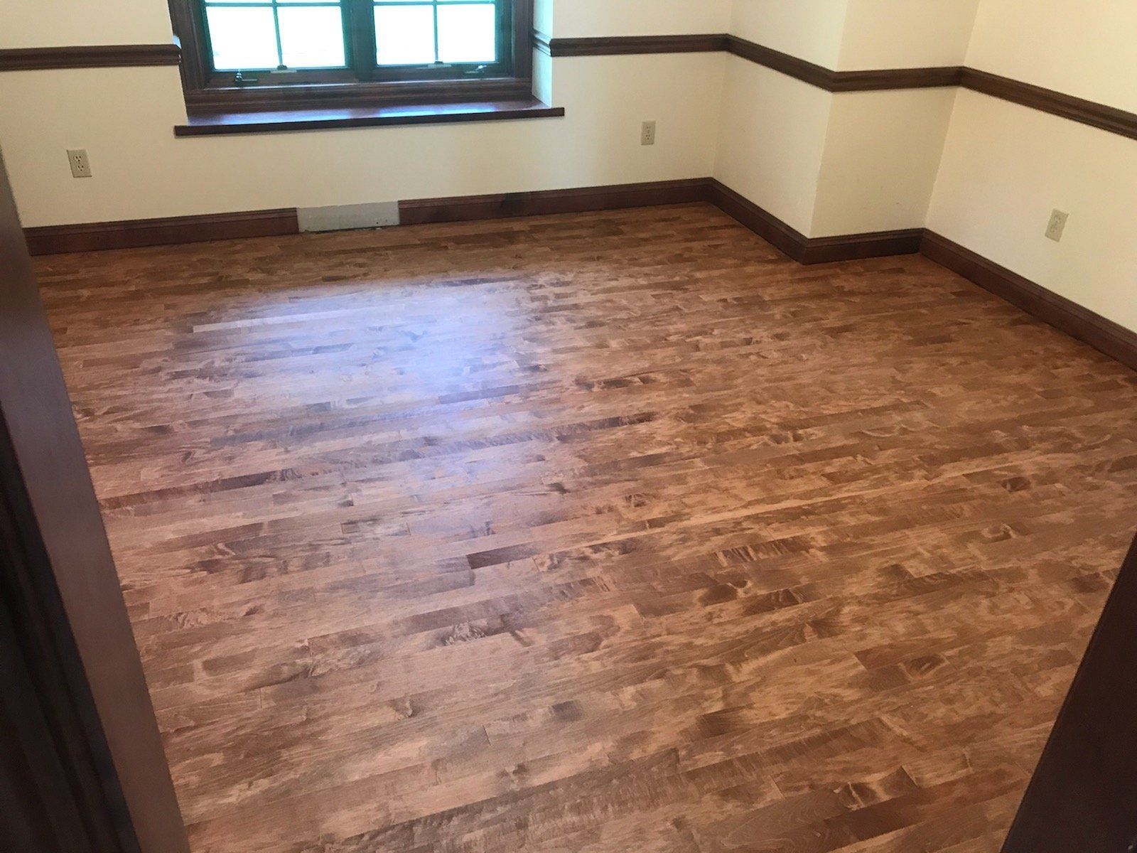 Empty room with wood flooring, white walls, and a window letting in natural light.