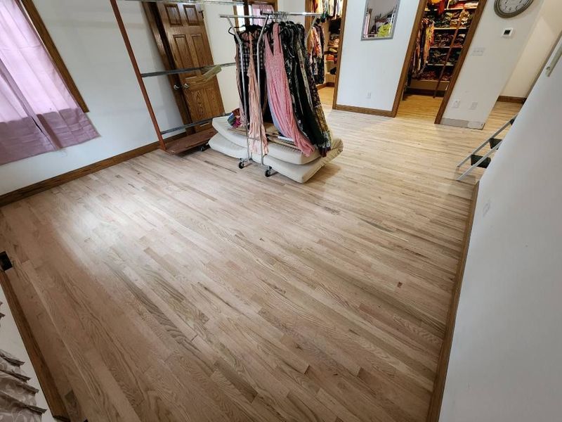 Empty room with light wood flooring, a clothes rack, and mirrors near an open doorway.