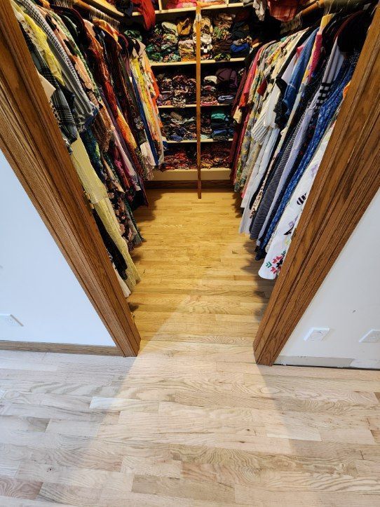 Open walk-in closet with colorful clothes on both sides and wood floor