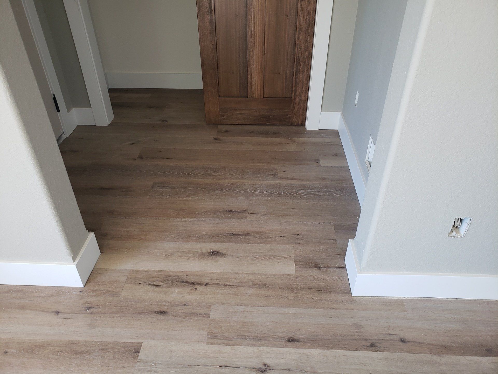 Empty hallway with light wood flooring, gray walls, and a wooden cabinet in the back wall.