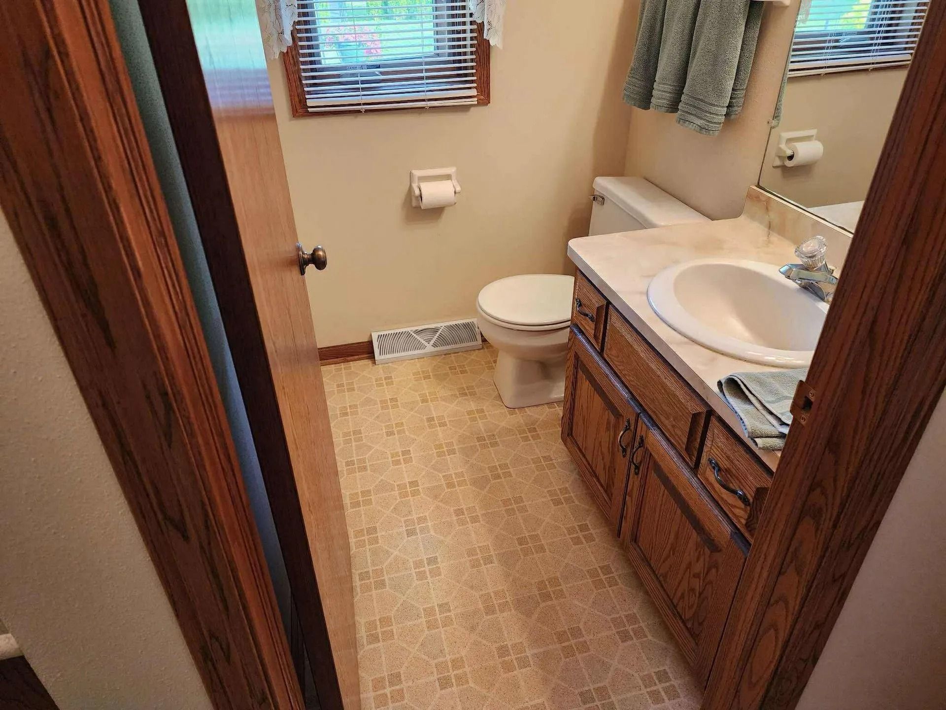 Small bathroom with a toilet, sink vanity, mirror, and two windows.