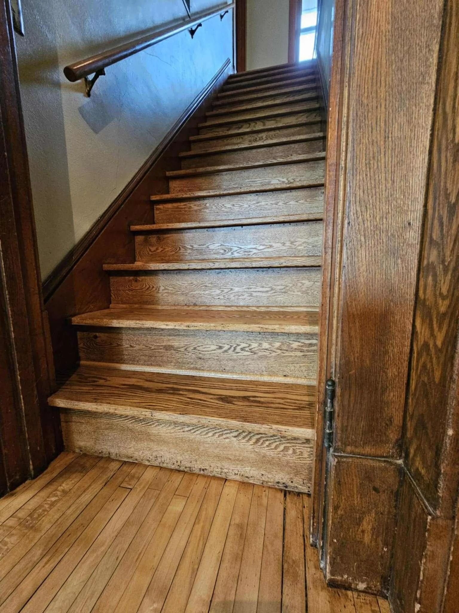 Wooden staircase in a rustic interior, with worn steps and a handrail leading upward.