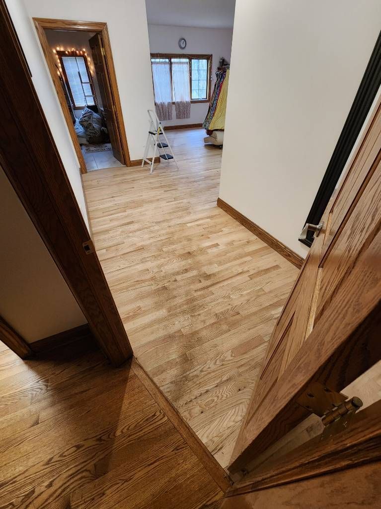 Open doorway to a wood-floored room with large windows and white walls