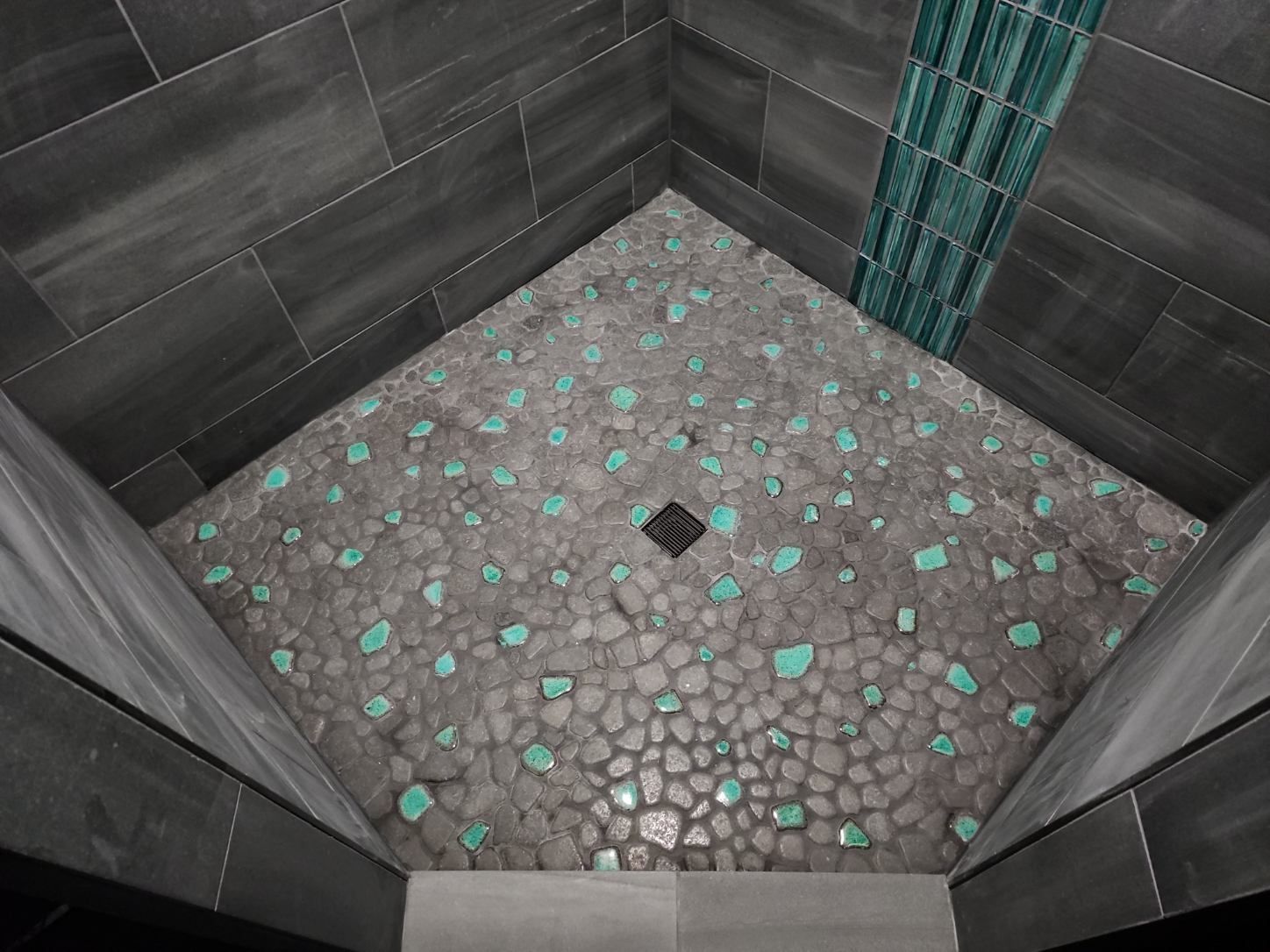 Small stone-floored shower room with dark tiled walls and a floor drain.