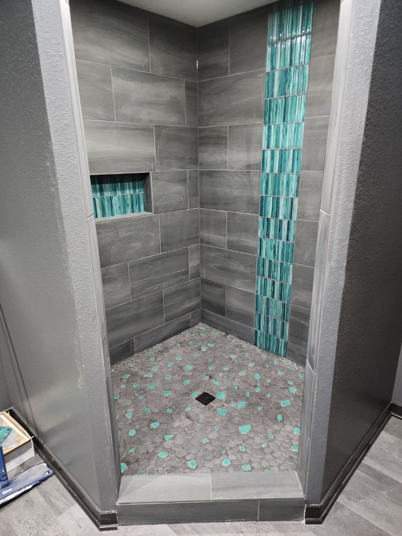 Gray tiled shower stall with turquoise mosaic accents and a small recessed shelf