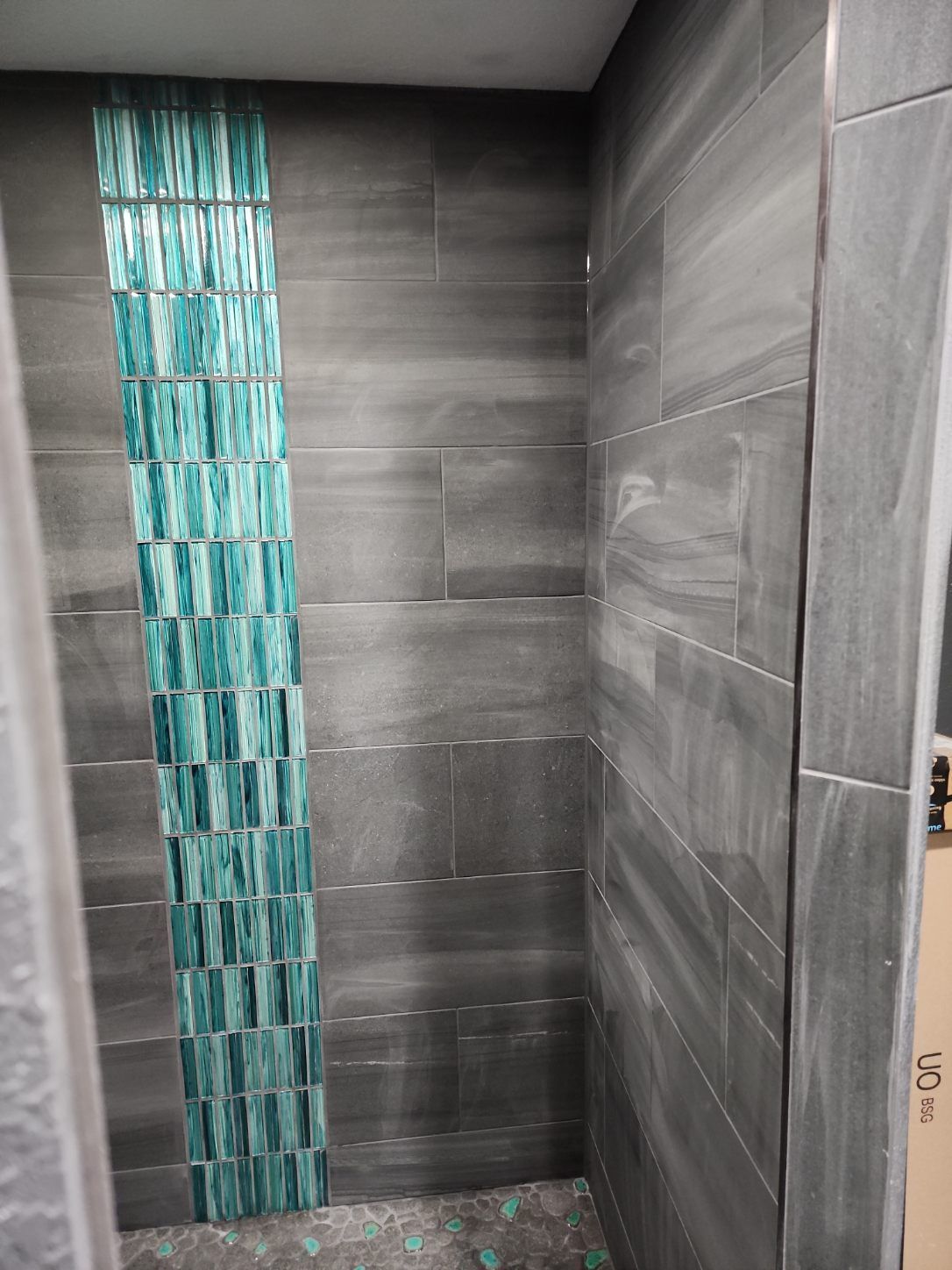 Gray tiled shower wall with a vertical strip of turquoise mosaic accent tiles