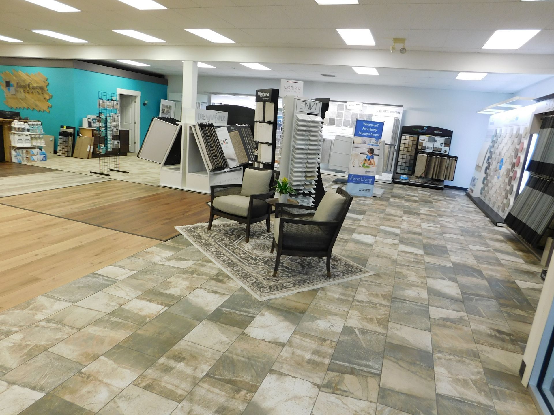 Spacious flooring showroom with display racks, sample tiles, and two chairs under bright ceiling lights.