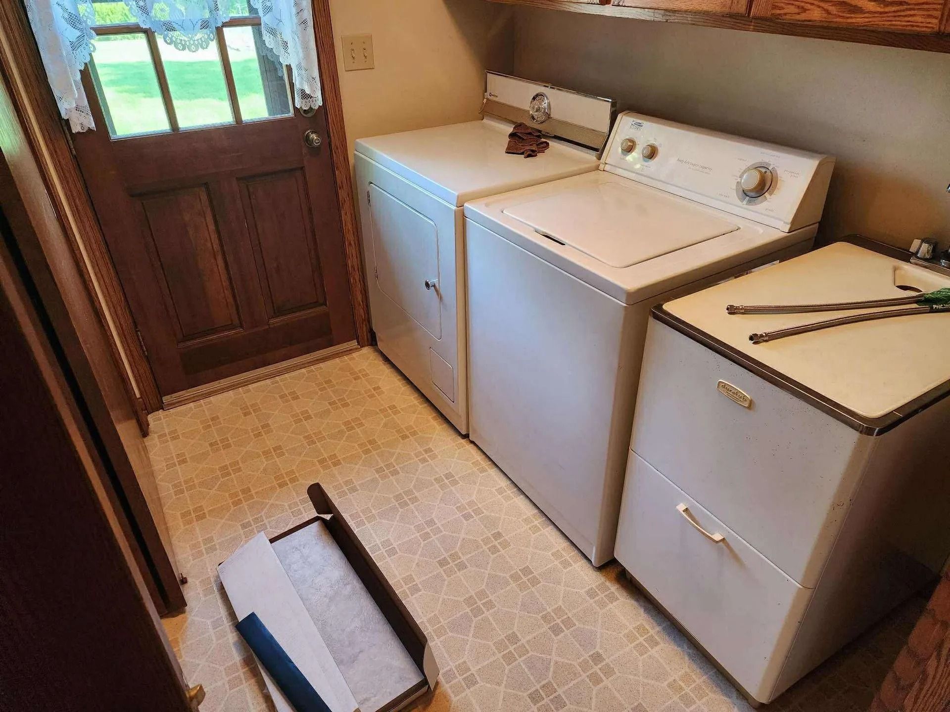 Small laundry room with washer, dryer, and utility sink beside a wooden door.