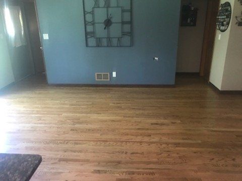 Empty living room with hardwood floor, blue walls, and wall decor near a doorway.