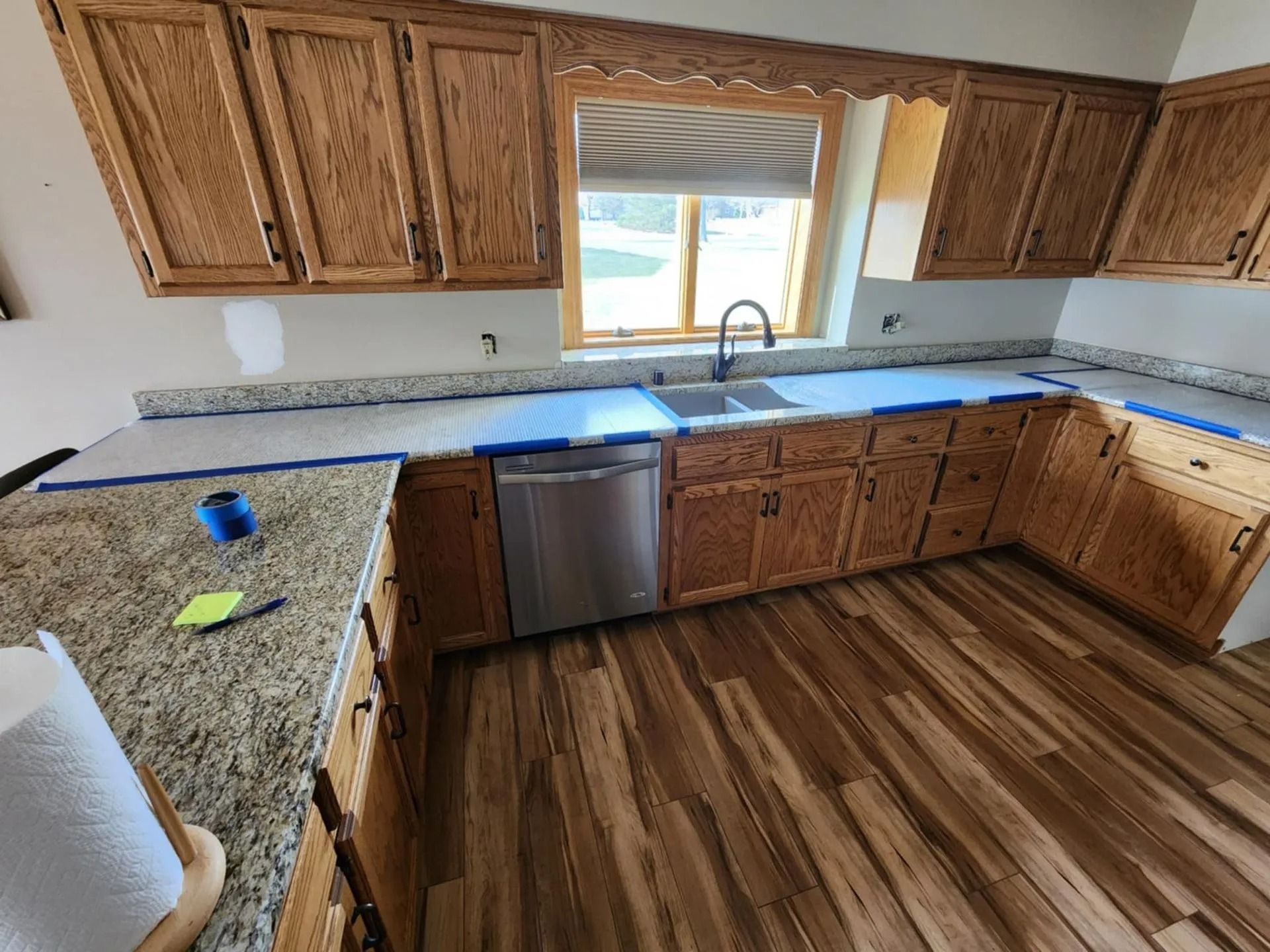 Kitchen with wood cabinets, granite counters, stainless dishwasher, and a window over the sink.
