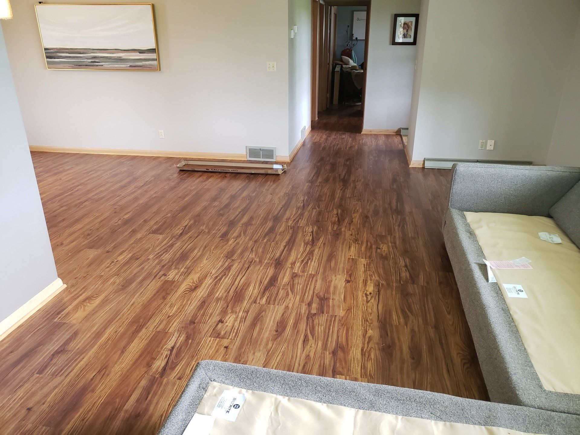 Empty living room with wood flooring, gray sofa, and doorway to a hall.