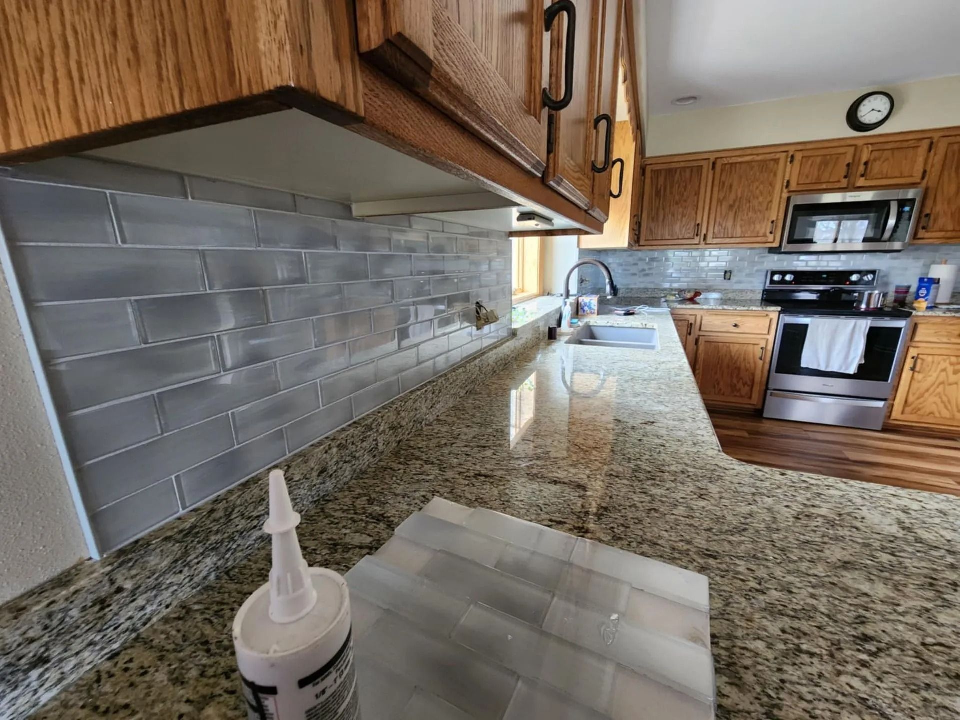 Kitchen countertop with granite counters, wood cabinets, white subway tile backsplash, and a stove in the background