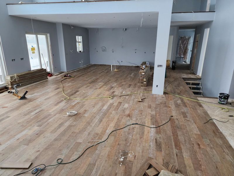 Renovation in progress in an empty room with unfinished wood flooring and exposed walls, with tools and cables on the floor