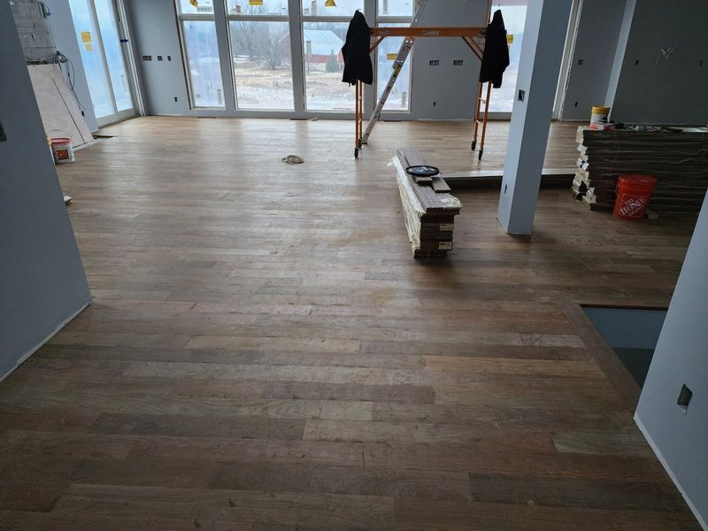 Empty room with wood floors, a person near glass doors, and stacked boards on the floor