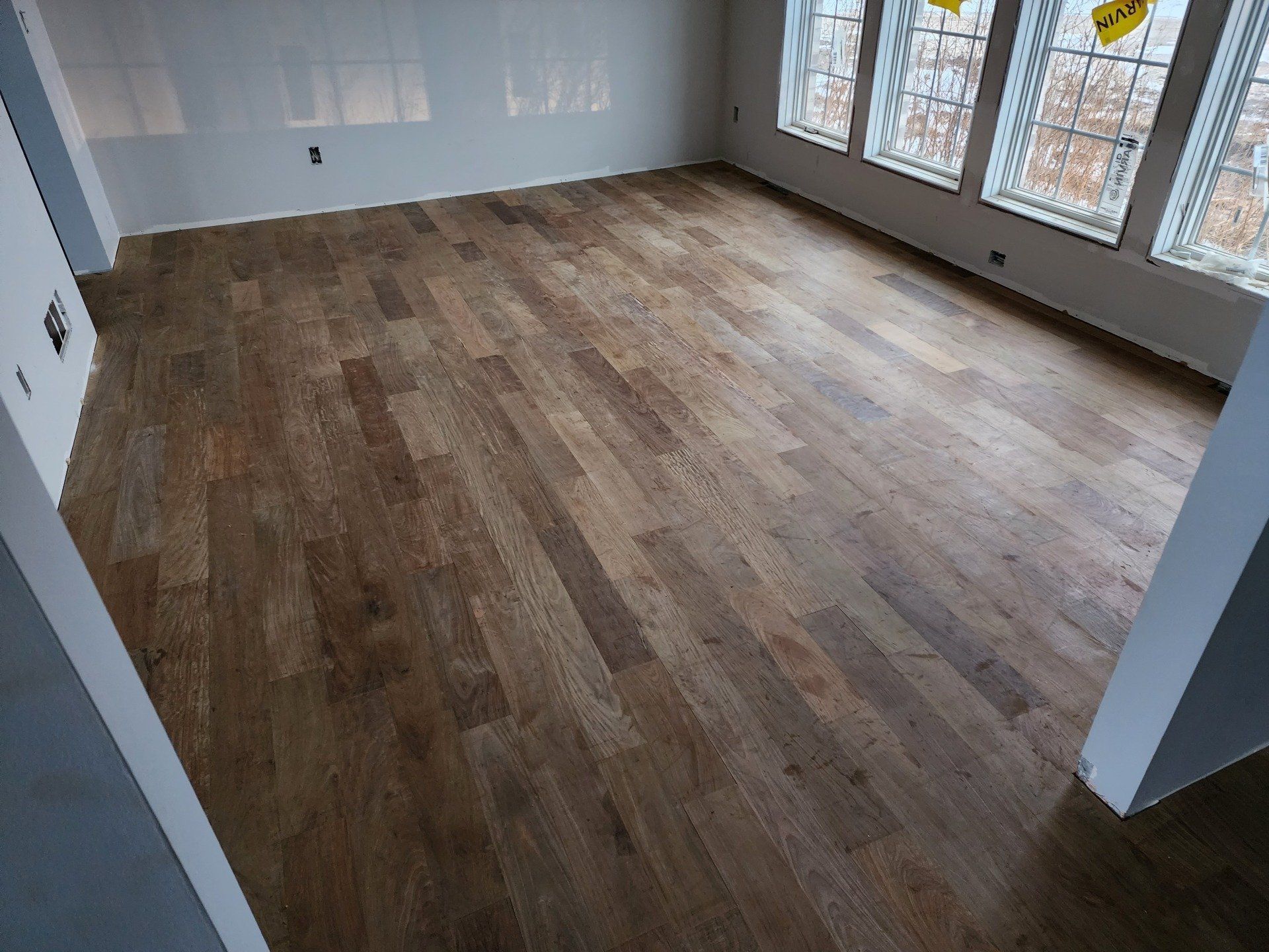 Empty room with light wood flooring, white walls, and large windows.
