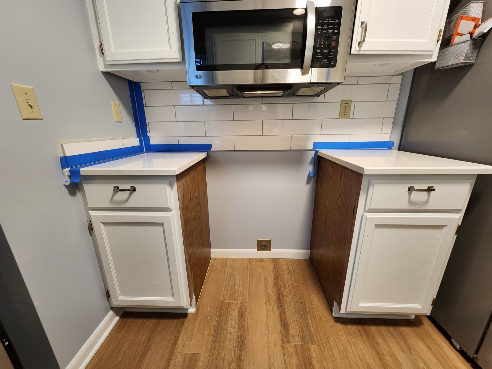 Compact kitchen nook with white cabinets, blue countertops, and a microwave above the counter.