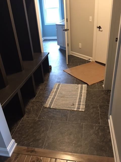Hallway with dark tile floor, built-in shelves, and a partially open door at the end; cardboard on the floor.