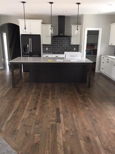 Modern kitchen with dark wood floors, black island, white cabinets, and stainless appliances