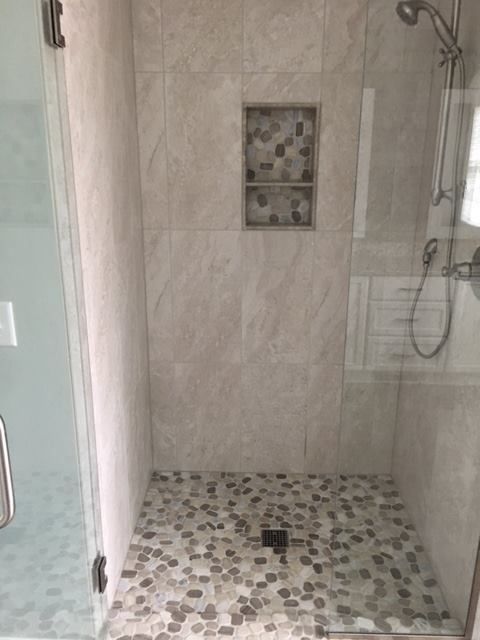 Small tiled walk-in shower with glass door and wall niche, viewed from the bathroom.