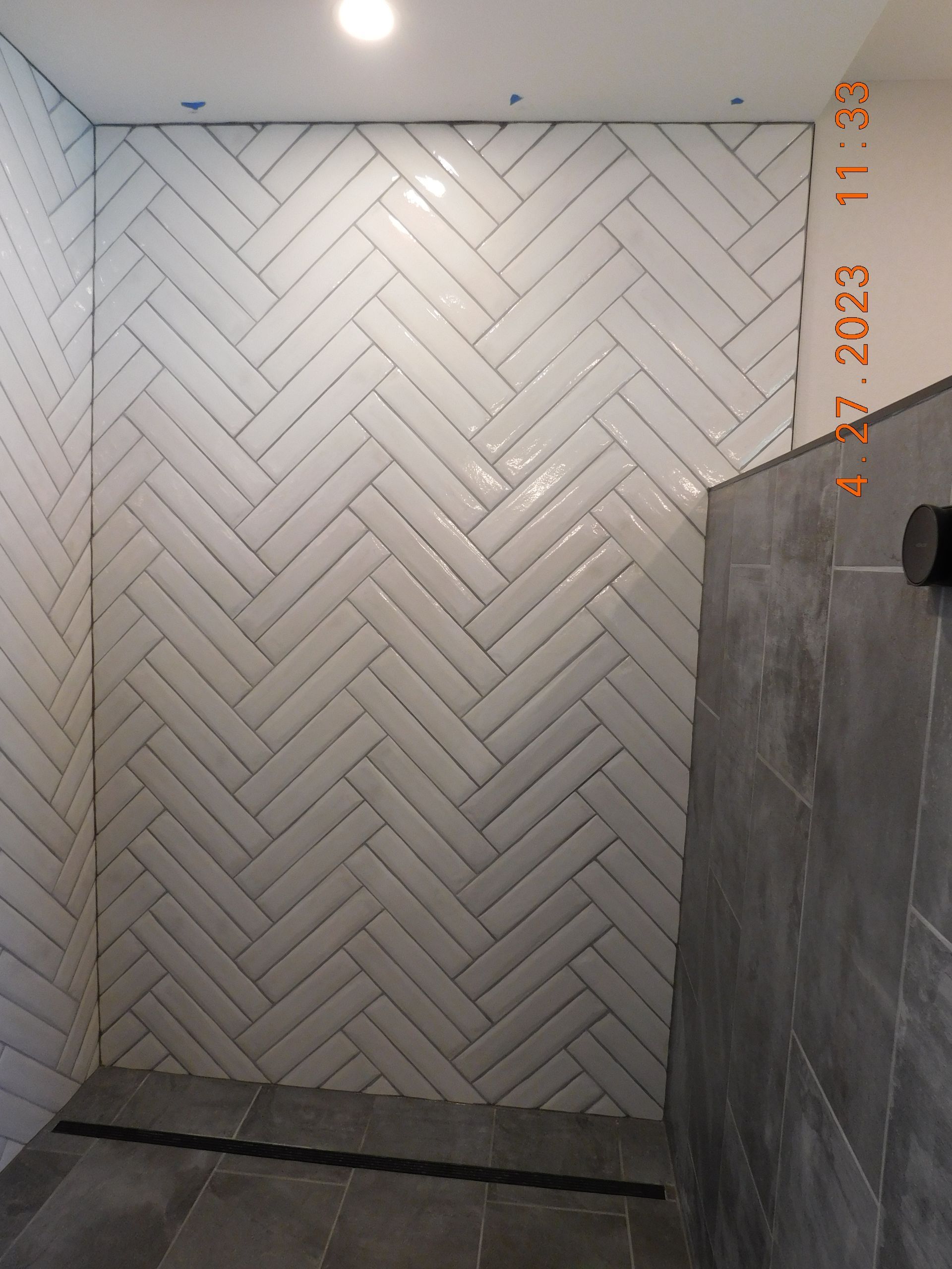 Small tiled shower alcove with white herringbone wall tiles, gray side wall, and recessed lights above