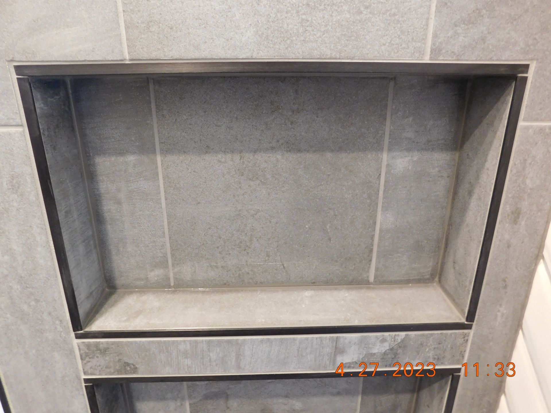Empty gray display shelf with a glass front and tiled back wall.